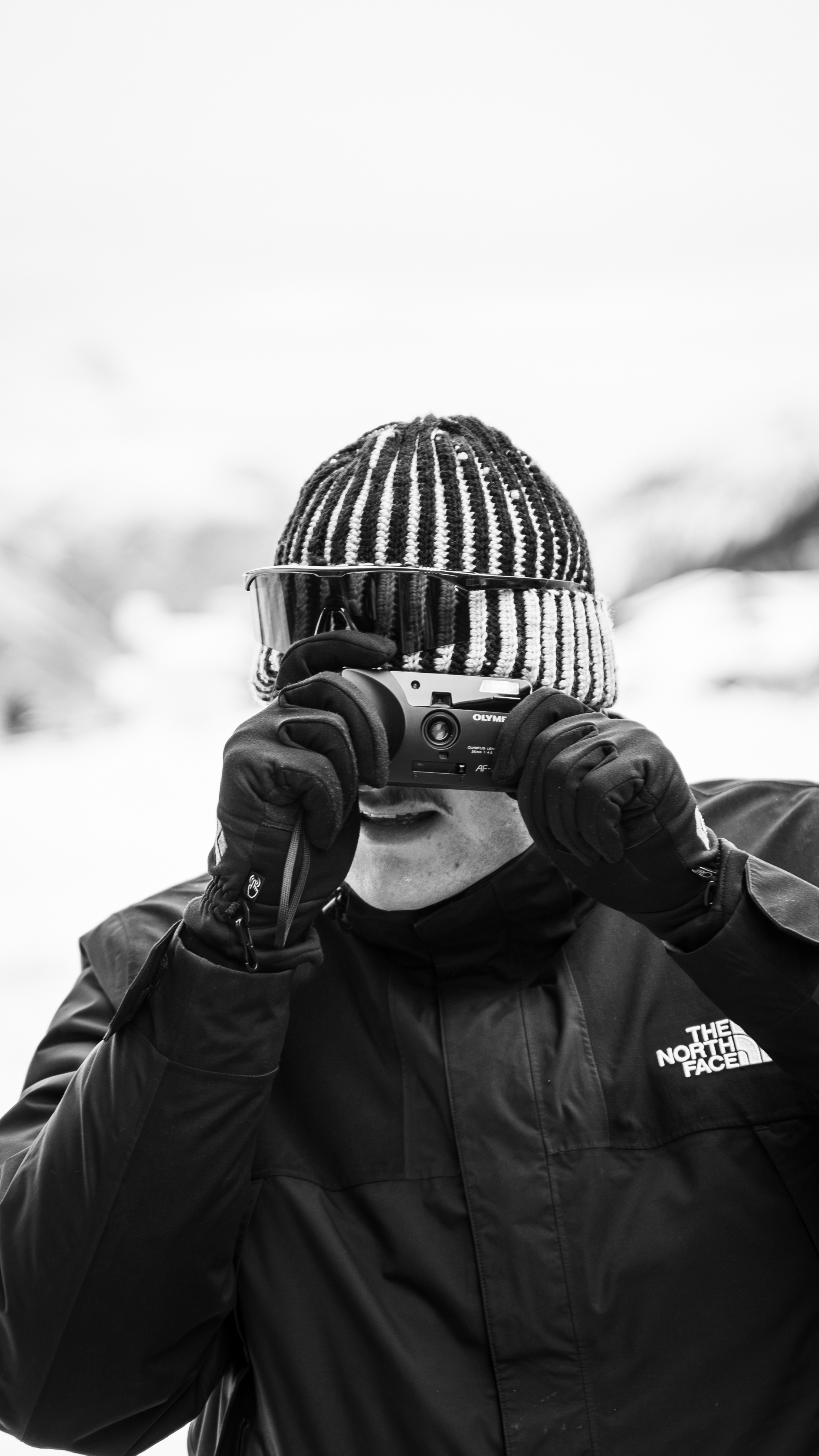 Alessandro Versiglia sulla neve, con berretto e occhiali, mentre fotografa con una fotocamera Olympus